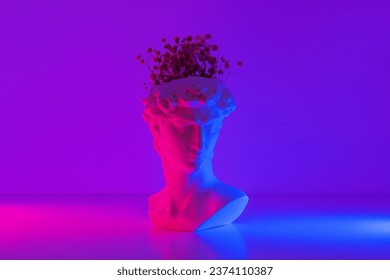 Plaster antique David's statue head with flowers inside pink and blue colored neon light. 3d trendy collage in magazine style. Contemporary art. Modern creative design