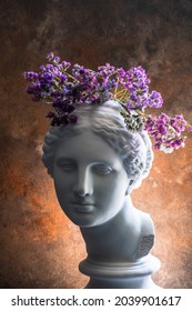 Plaster bust of the beautiful Aphrodite with flowers on her head on a rusty antique background. A beautiful play of light.