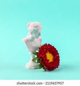 Plaster bust of venus with a flower on blue background.