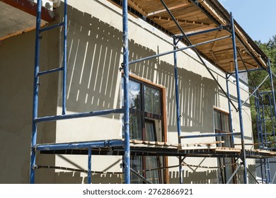 Plaster coating on facade insulation, external wall scaffolded for finishing, construction phase, smoothing render, surface preparation, house renovation works.
