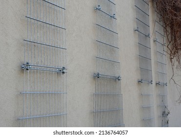 plaster concrete wall on a house or factory. on the wall are attached galvanized grilles made of cheap mesh, which are full of climbing plants that green the monotonous wall. Garage wall of the house 