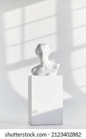 The Plaster Head Of An Antique Girl Stands On A Pedestal On A White Background