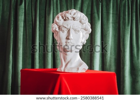 Plaster head of David on a red podium against a background of green curtains