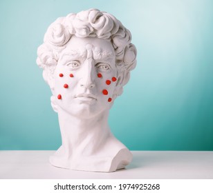 Plaster head statue with red pimples made of plasticine.Problem skin concept on blue background.