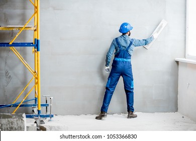 Plasterer in blue working uniform plastering the wall indoors