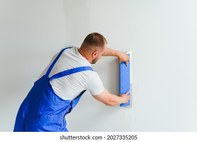 Plasterer smoothes the wall surface with a wall grinder. Master builder grind a white plaster wall. a man in overalls grinds the surface in a respirator. experienced repairman