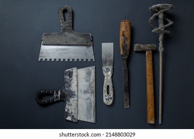 Plasterer's Tool In Plaster. Set Of Dirty Tools For Plastering Work. Flat Lay Tools. Spatula, Hammer, Whisk And Chisel Lie On The Concrete.