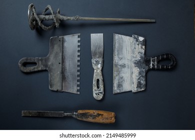 Plasterer's Tool In Plaster. Set Of Dirty Tools For Plastering Work. Flat Lay Tools. Spatula, Hammer, Whisk And Chisel Lie On The Concrete.