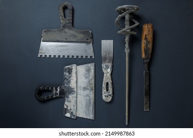 Plasterer's Tool In Plaster. Set Of Dirty Tools For Plastering Work. Flat Lay Tools. Spatula, Hammer, Whisk And Chisel Lie On The Concrete.