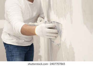 Plasterwork and wall painting preparation. Asian male applying plaster or filling drywall patch	
