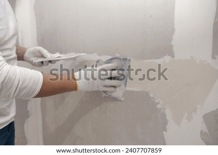Plasterwork and wall painting preparation. Asian male applying plaster or filling drywall patch	
