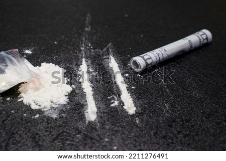 Plastic bag, two lines and a bunch of cocaine with a breathing tube with hundred dollar bill, on a black background, closeup.