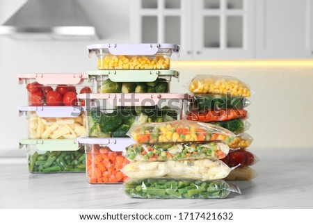 Plastic bags and containers with different frozen vegetables on white marble table in kitchen