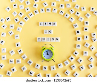 Plastic block cube with word TIME TO THINK and around scattered individual letters and alarm clock on yellow background. Personal development and career growth or change attitude yourself concept.
