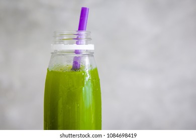 Plastic bottle of cold-pressed green juice with purple straw against gray wall. Body cleance, fast, detox concept. Minimalism food photography. Copyspace