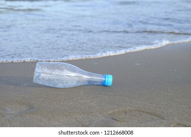 A plastic bottle of drinking water littering on the beach with sea waves background for an environmental cleaning concept  - Shutterstock ID 1212668008