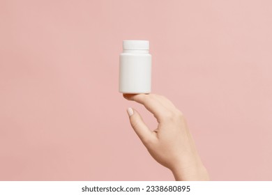 Plastic bottle (tube) in hand on a pink background. Packaging for vitamins, tablets or capsule, or supplement - Shutterstock ID 2338680895