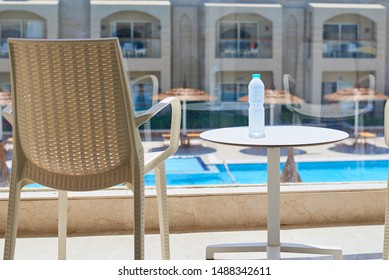 Plastic Bottle Of Water And Empty Chair On Balcony Against Swimming Pool Background