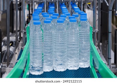 Plastic bottles with blue caps on conveyor belt in water bottling factory. Industrial production line for bottled water manufacturer. - Powered by Shutterstock