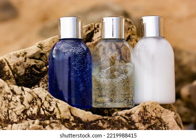 Plastic Bottles With Natural Cosmetic In Travel Containers - Blue Shower Gel, Shampoo With Bubbles Inside, Body Lotion In Miniature Containers Against A Brown Stone Rock Background. Face Body Care. 