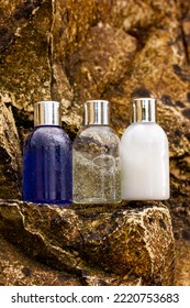 Plastic Bottles With Natural Cosmetic In Travel Containers - Shower Gel, Shampoo With Bubbles Inside, Body Lotion In Miniature Containers Against A Rock Background. Face Body Care Vertical Photo. 