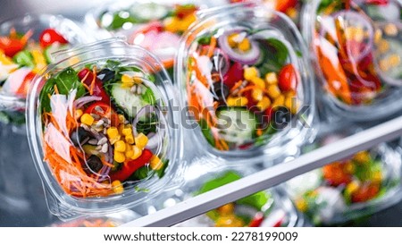 Plastic boxes with pre-packaged vegetable salads, put up for sale in a commercial refrigerator
