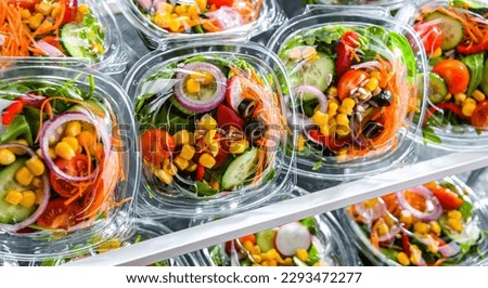 Plastic boxes with pre-packaged vegetable salads, put up for sale in a commercial refrigerator