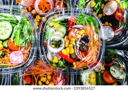 Plastic boxes with pre-packaged vegetable salads, put up for sale in a commercial refrigerator