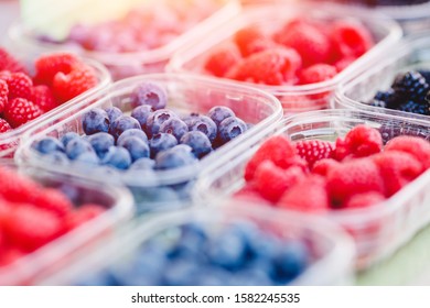 Plastic boxes with raspberries, blueberries, blackberries on counter of market store.