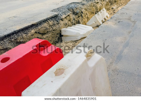 Plastic bright construction barrier near the\
trench, road works. Focus on\
foreground.