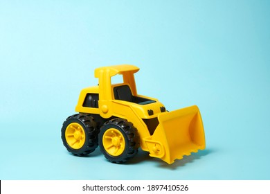 Plastic Bulldozer Toy With A Raised Front On A Cyan Background                             