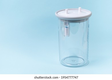 Plastic Canister From Medical Suction Machine On Blue Backdrop. Part Of Portable Aspirator Used To Remove Mucus, Blood, Bodily Fluids From Patient. Medical Equipment Using In Ambulances 