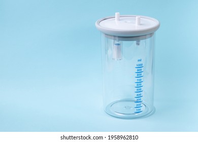 Plastic Canister From Medical Suction Machine On Blue Backdrop. Part Of Portable Aspirator Used To Remove Mucus, Blood, Bodily Fluids From Patient. Medical Equipment Using In Ambulances 