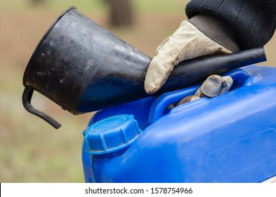 Plastic Canister And Watering Can For Diesel In Hand. Hand In Protective Glove Holding The Canister With The Fuel And The Filler Funnel. Side View. Shot At Eye Level.	