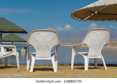 Plastic Chairs On Beach Of Salty Lake In World Dead Sea, Full Of Minerals Near Luxury Vacation Resort Ein Bokek, Perfect Place For Medical Treatments, Climatotherapy, Thalassotherapy And Heliotherapy.