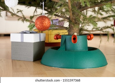 Plastic Christmas Tree Stand Surrounded By Gift Boxes Stands At Home In New Year Eve On The Floor In City Flat.  Real Organic Christmas Tree At Home.