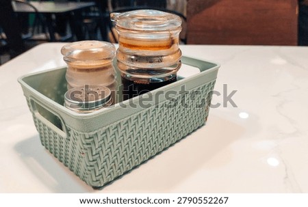 A plastic condiment container with an elegant engraved design, containing soy sauce, pepper, and salt, is placed on the table