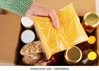 Plastic Container With Corn Grits In Female Hand On Emergency Food Box Background