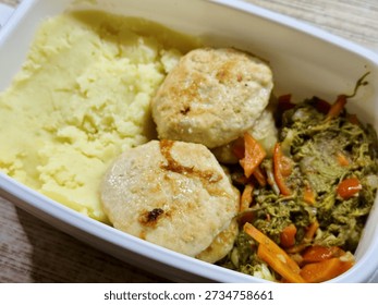 Plastic Container With Mashed Potatoes, Two PanFried Cutlets And SautEd Carrots And Greens On Wooden Desk, Midday Office Setting With Natural Light, BudgetFriendly Homemade Reheatable
