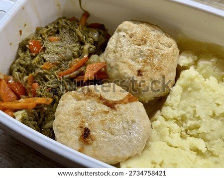 Plastic Container With Mashed Potatoes, Two PanFried Cutlets And SautEd Carrots And Greens On Wooden Desk, Midday Office Setting With Natural Light, BudgetFriendly Homemade Reheatable