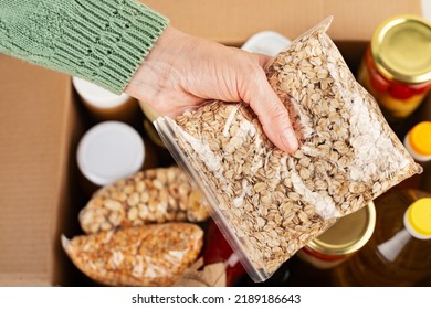 Plastic Container With Rolled Oats In Female Hand On Emergency Food Box Background