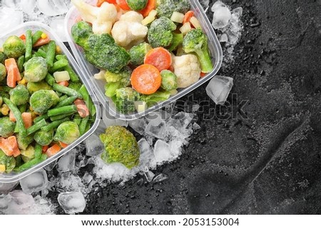 Plastic containers with frozen vegetables and ice on dark background