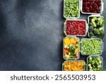 Plastic containers with frozen vegetables. Top view. On a gray stone background. Winter supplies of food.