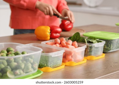 Plastic containers with vegetables for freezing on wooden table and woman on background
