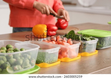 Plastic containers with vegetables for freezing on wooden table and woman on background