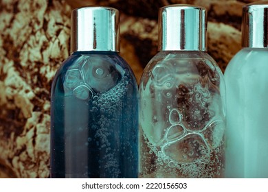 Plastic Cosmetic Bottles With Natural Cosmetic In Travel Containers - Shower Gel, Shampoo With Bubbles Inside, Body Lotion In Miniature Containers Against A Rock Background Close Up. Face Body Care.