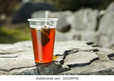 Plastic Cup With Black Tea On Big Stone Over Nature Background.