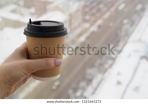 Plastic cup with fresh hot coffee in woman\'s hand\
on the background of central street of Voronezh, Russia. View from\
high floor