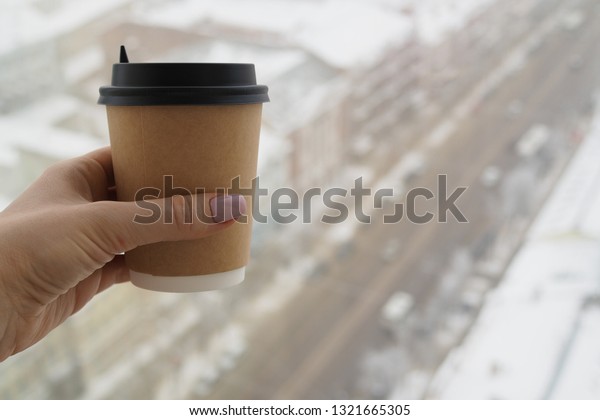 Plastic cup with fresh hot coffee in woman's hand
on the background of central street of Voronezh, Russia. View from
high floor