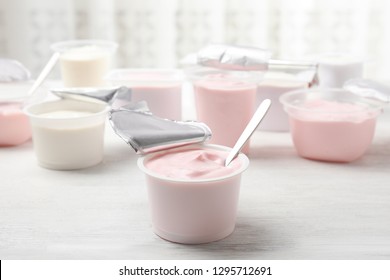 Plastic cup with fresh yogurt and spoon on white wooden table